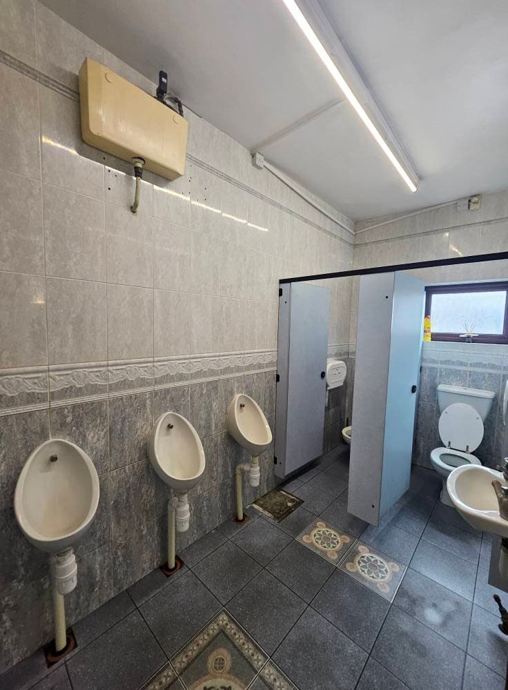 Men's washroom with a row of urinals and cubicles cleaned across the tiled walls and patterned floor