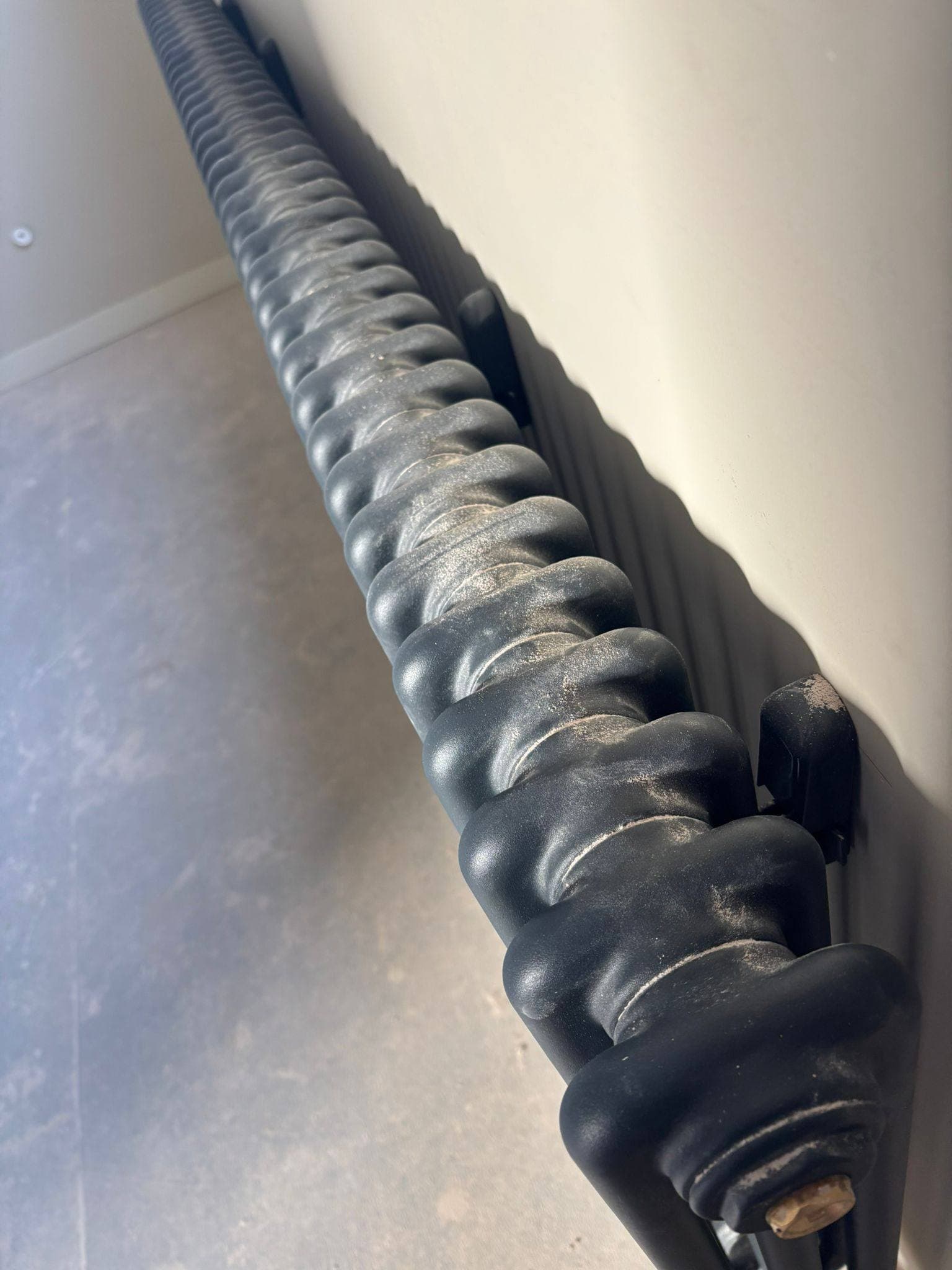 Black column radiator covered in plaster dust after building work