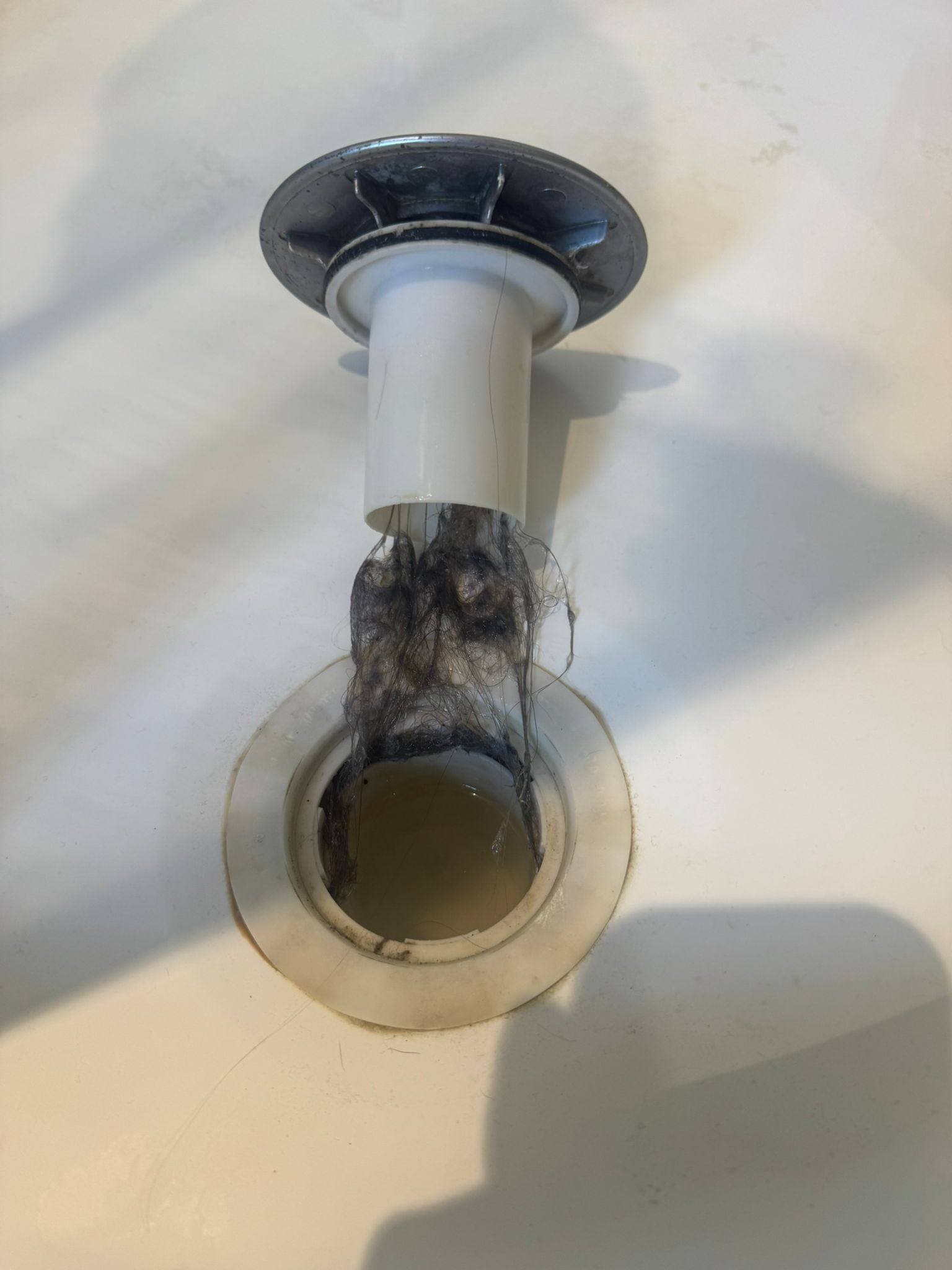 Bathroom sink plug pulled out with matted hair and gunge wrapped around the stem