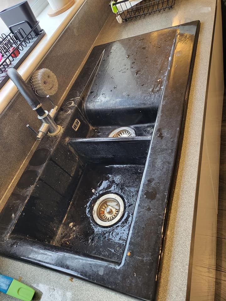 Black composite kitchen sink dulled with grease, water marks and food debris