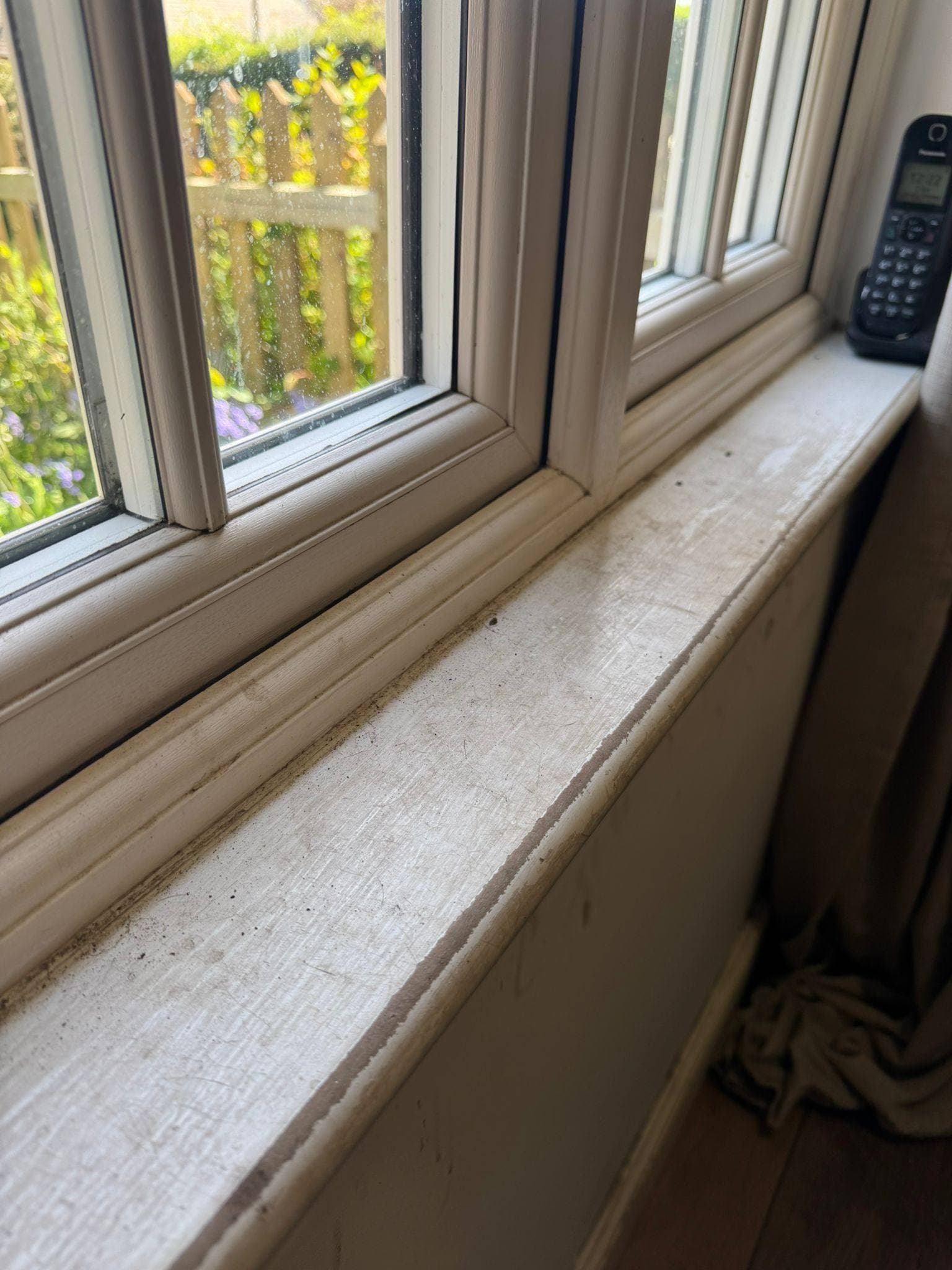 Painted window sill marked with dust, grime and debris along the frame
