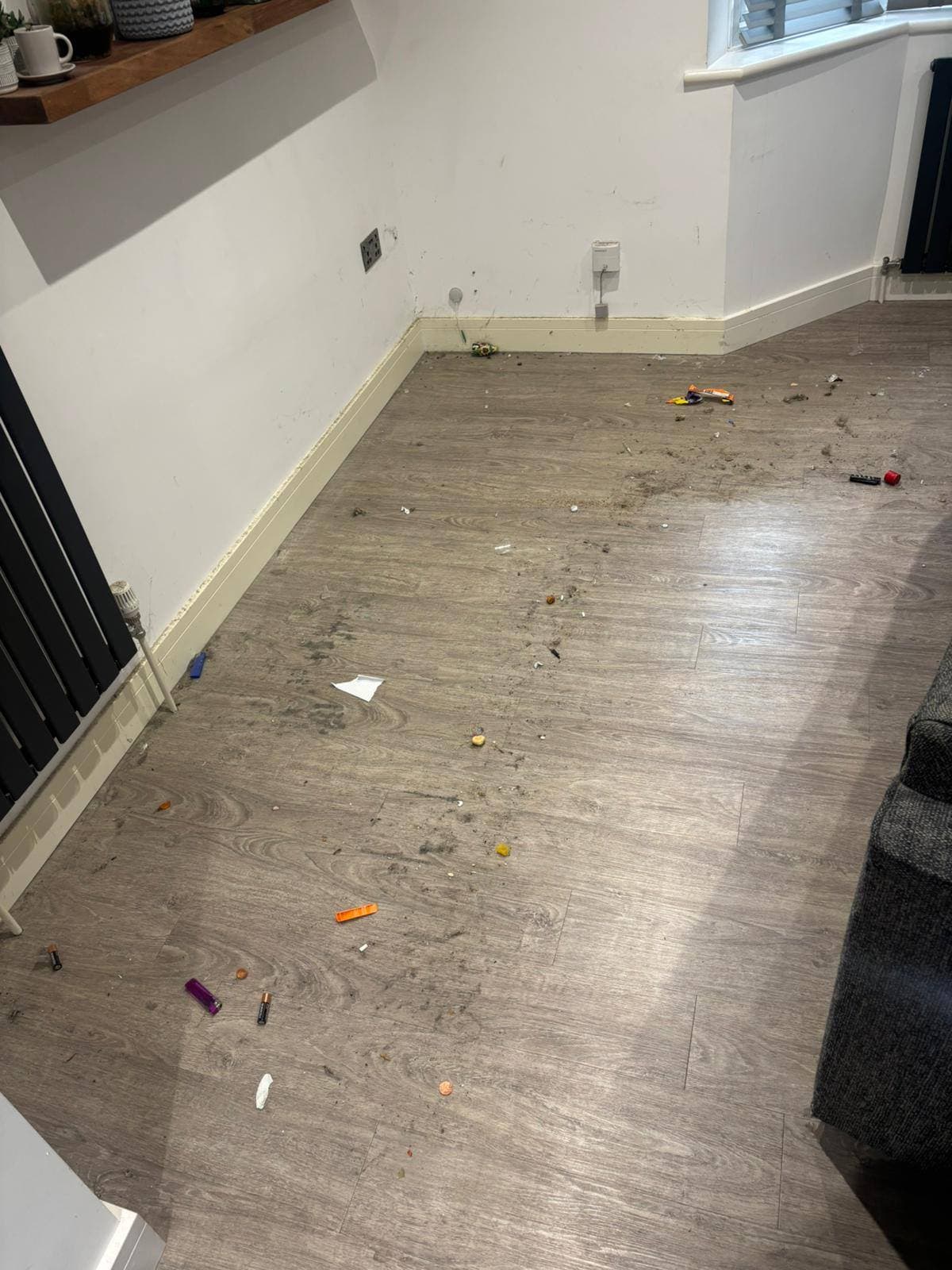 Grey wood-effect floor scattered with crumbs, debris and bits of rubbish before cleaning