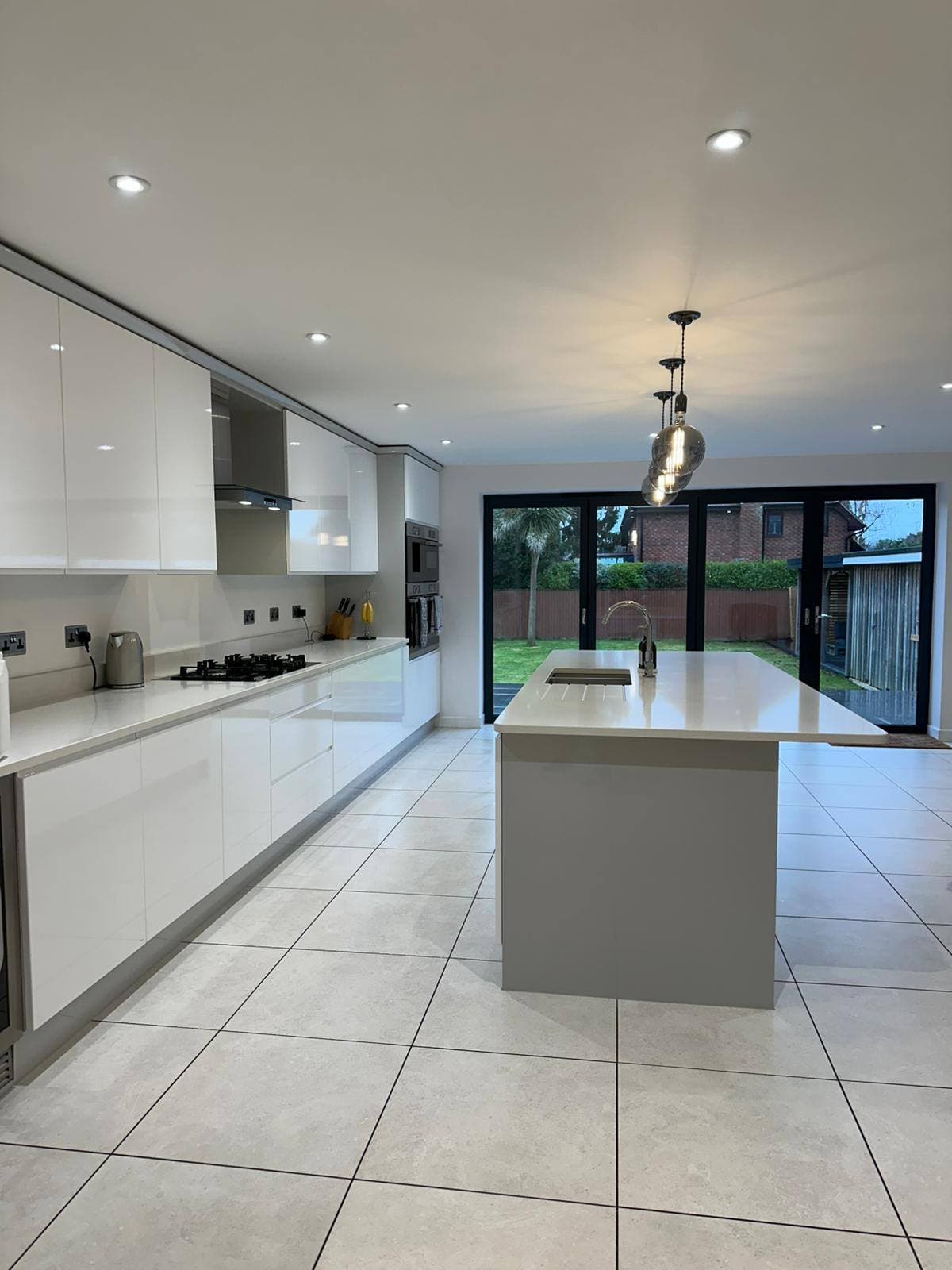 Large white gloss kitchen with spotless floor tiles and worktops