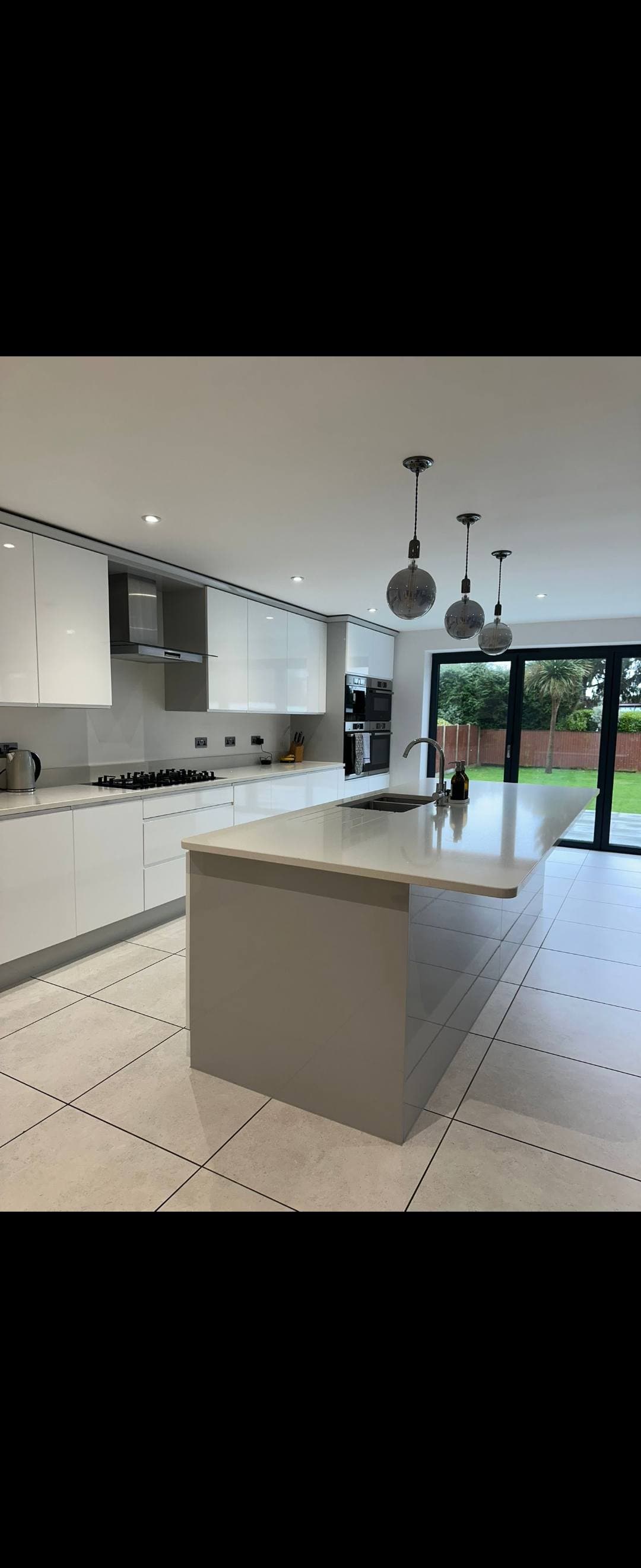 Large white gloss kitchen with a stone-topped island, gleaming tiled floor and bifold doors after cleaning